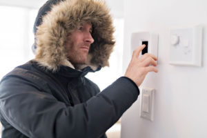 A man wearing a winter coat adjusting a thermostat.
