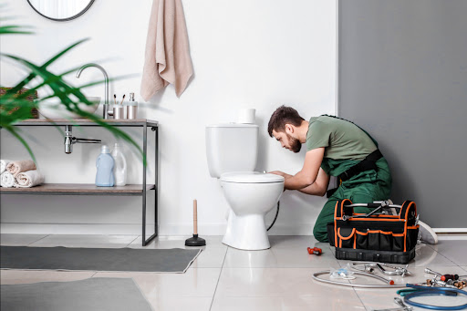A plumber repairing a toilet in a residential bathroom.