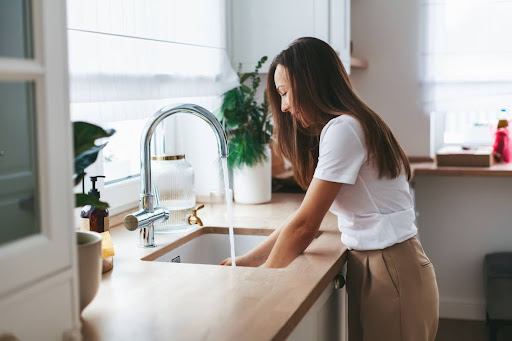 A woman using a kitchen sink faucet.