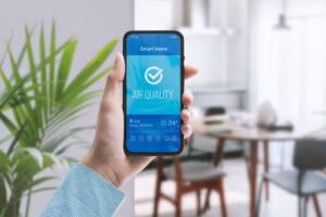 A close-up of a hand holding a phone that says "air quality." There is a kitchen in the background.