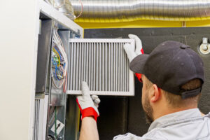 A man replacing a furnace air filter during furnace maintenance.