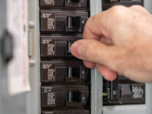 A close-up of a hand resetting a tripped circuit breaker on an electrical panel.