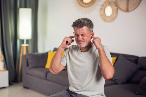 A man blocking his ears with his fingers due to a loud noise in his home.